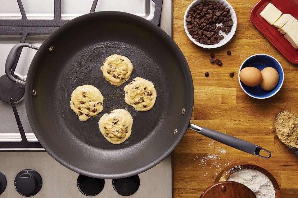 Chocolate chip cookies cooking on an Anolon skillet with ingredients on the counter