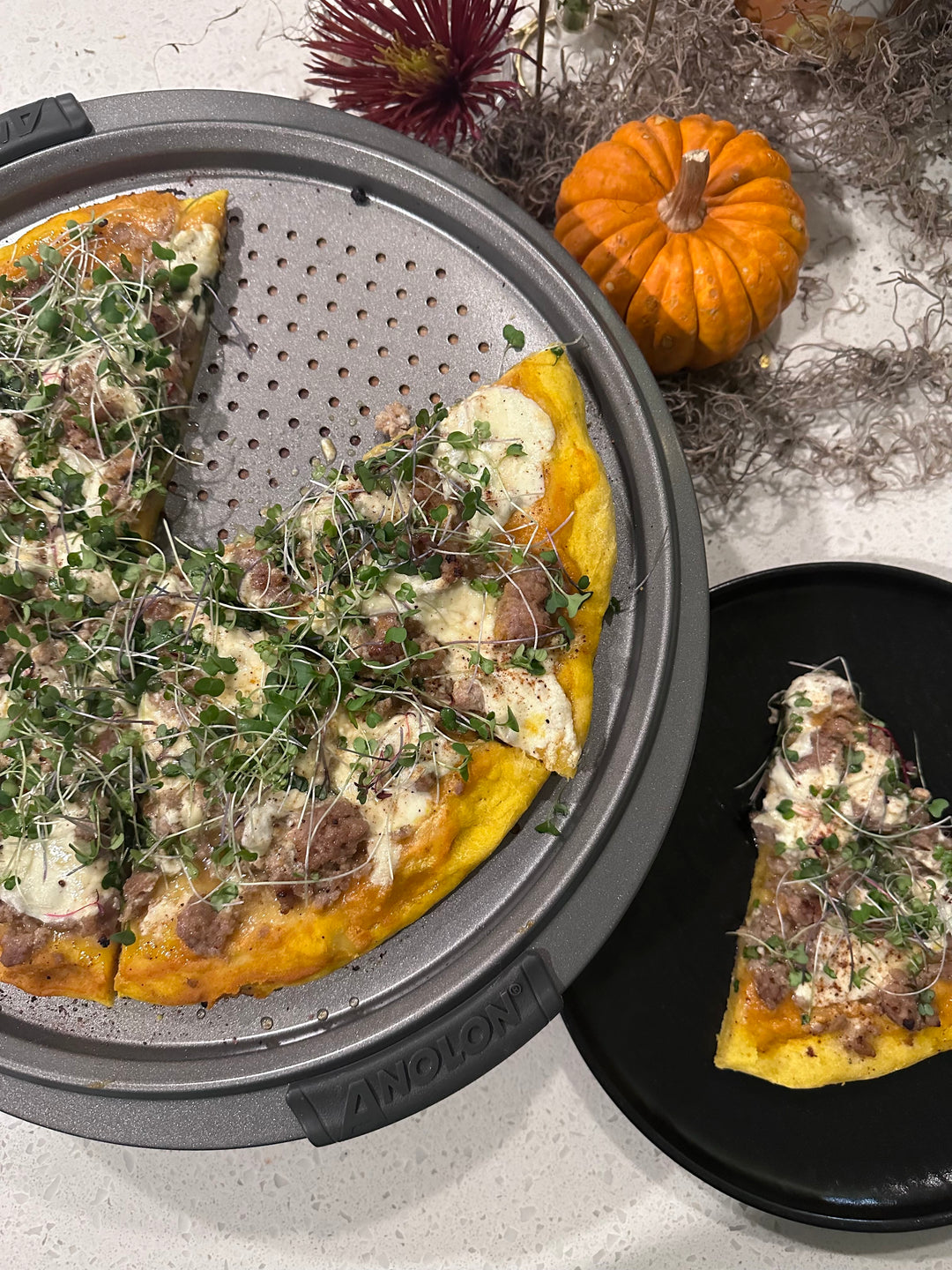 Maple sausage pizza on an Anolon pizza crisper pan with fall decor on countertop