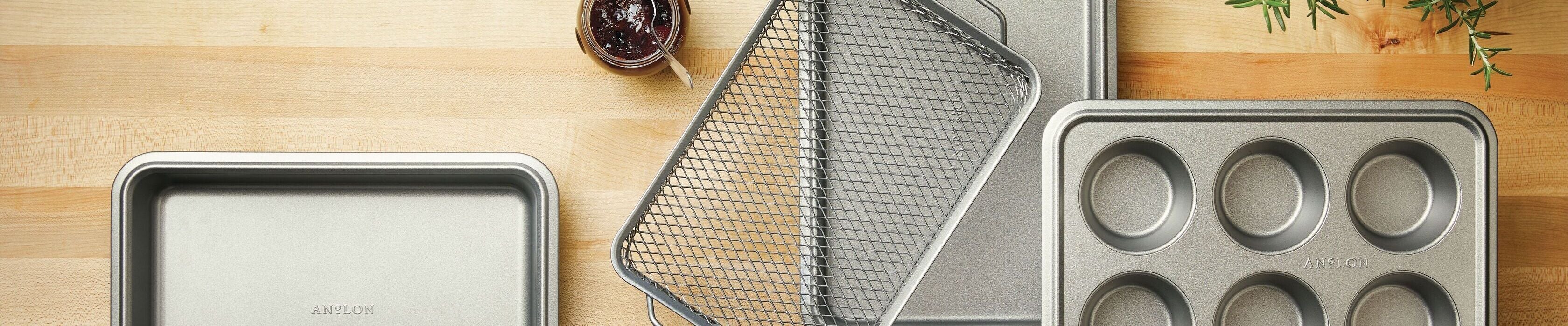 A top view of a table with baked goods: a bundt cake, chocolate cookies on a tray, cream-filled cookies, and a pizza in a pan. Theres also a bonsai, glasses of drinks, and an orange napkin.