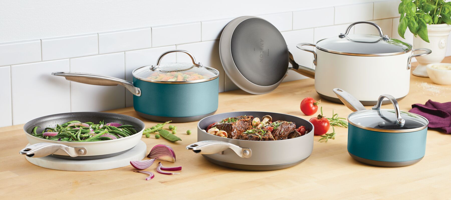 A kitchen scene with various pots and pans cooking different foods on a wooden countertop. Vegetables, herbs, and a garlic bulb are scattered around. A tiled backsplash and sunlight are visible.