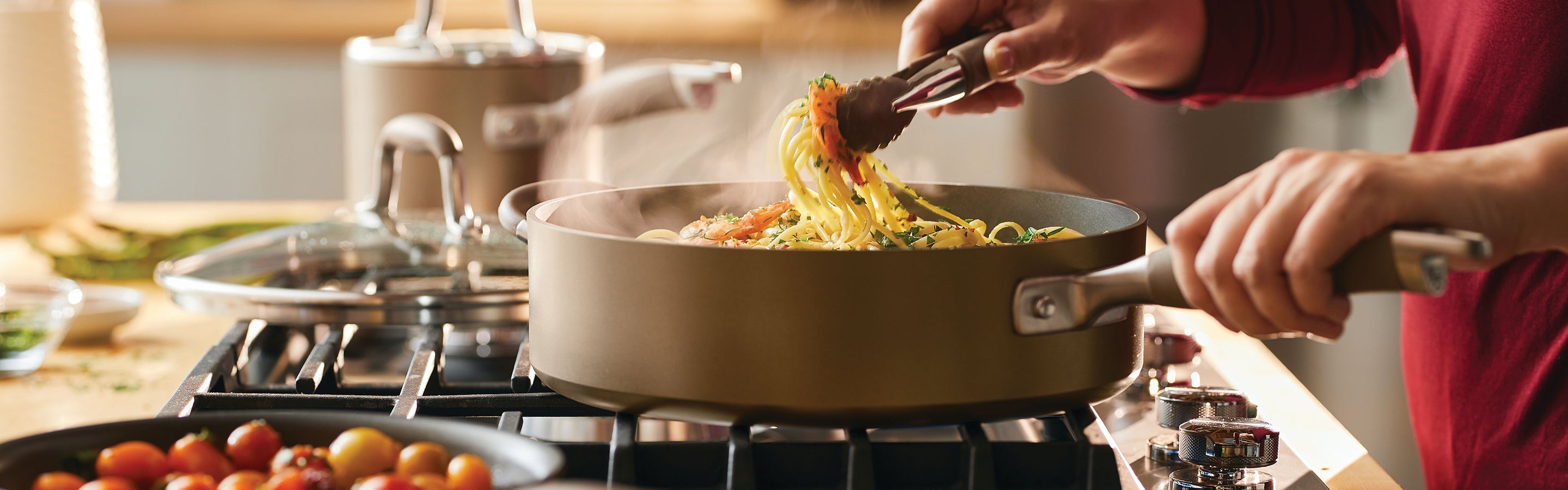 Three stainless steel pans hang on a hexagonal white tiled wall. Each pan displays a circular emblem on its base, reflecting light. The arrangement showcases various sizes of cookware.