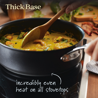 Someone stirs a thick, yellow curry with vegetables and chicken in a black pot on a stovetop. Text reads Thick Base, incredibly even heat on all stovetops, and oven safe to 500°F, with an arrow pointing to the Anolon X 3.5-Quart Hybrid Nonstick Induction Sauté Pan with Lids base.