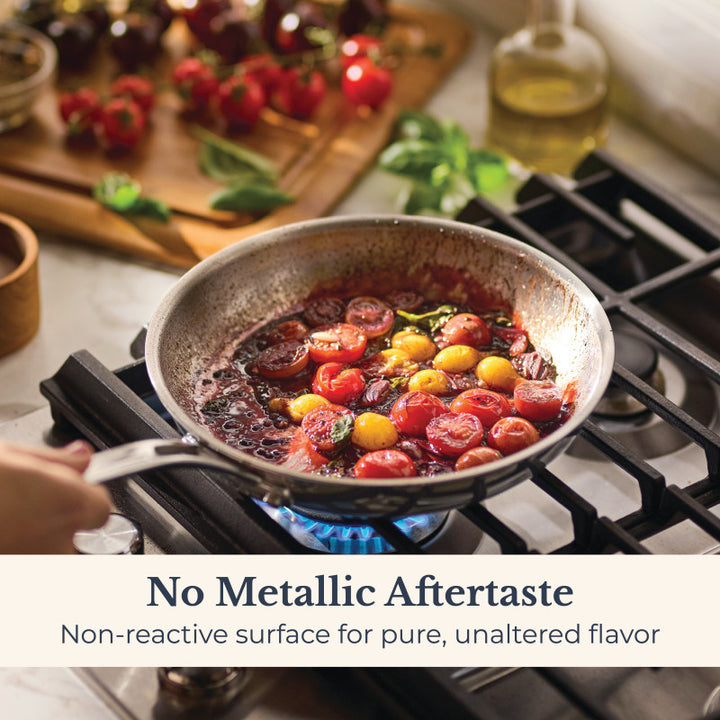 An EverLast Tri-Ply Clad Stainless Steel 10-Piece Cookware Set skillet cooks cherry tomatoes in sauce over a stove. Text: No Metallic Aftertaste—non-reactive surface preserves pure flavor. Fresh tomatoes and herbs appear in the background.