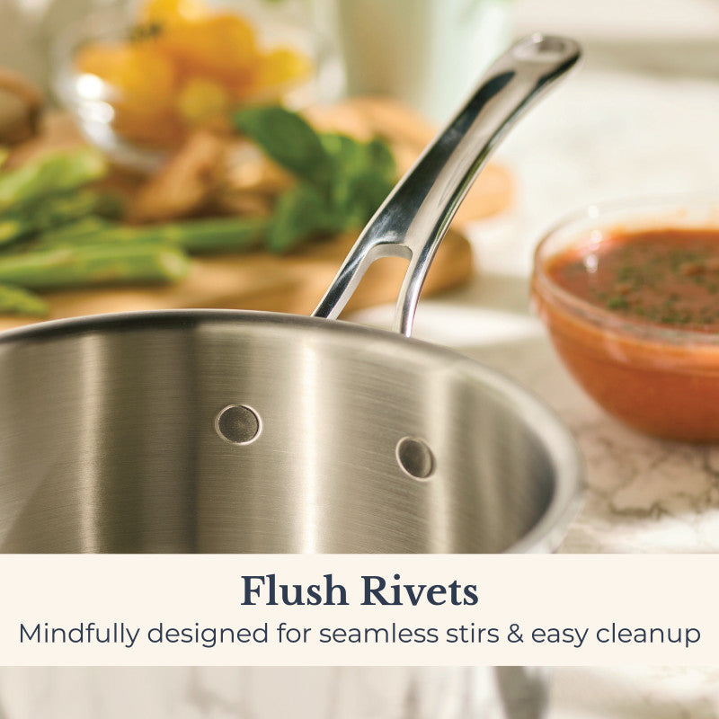 A close-up of the EverLast Tri-Ply Clad Stainless Steel 3-Quart Saucepan with Lid, featuring interior flush rivets, sits on a marble counter near tomato sauce and fresh vegetables. Text: “Flush Rivets. Designed for seamless stirs & easy cleanup.”.