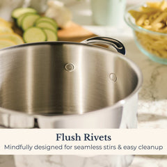 A close-up of the EverLast Tri-Ply Clad Stainless Steel 8-Quart Stockpot with Lid shows flush rivets on its inner wall. Blurred sliced vegetables and pasta appear in the background. Text reads: Flush Rivets—Seamless stirs & easy cleanup.