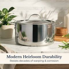 An EverLast Tri-Ply Clad Stainless Steel 8-Quart Stockpot with Lid rests on a white counter among green plants and kitchen items. Text below: Modern Heirloom Durability—Resists decades of warping & corrosion.