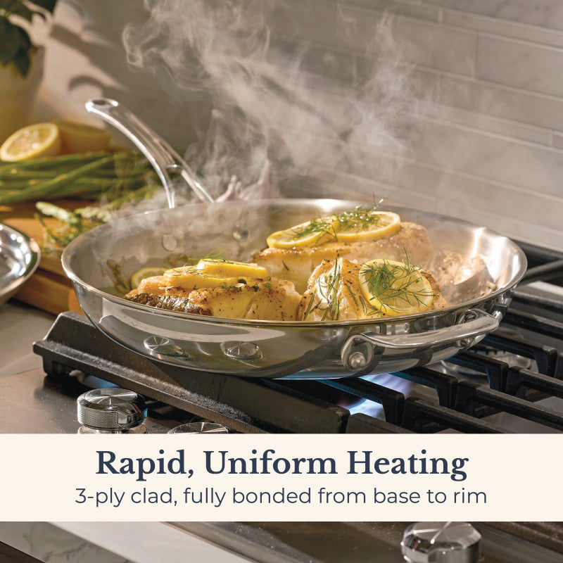 An EverLast Tri-Ply Clad Stainless Steel 12.5-Inch Frying Pan with Lid and Helper Handle cooks chicken breasts topped with lemon and herbs on the stove, steam rising. Rapid, uniform heating—designed for passionate home chefs.