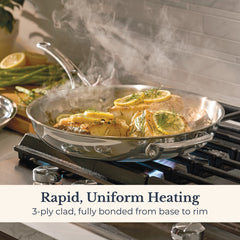 An EverLast Tri-Ply Clad Stainless Steel 12.5-Inch Frying Pan with Lid and Helper Handle cooks chicken breasts topped with lemon and herbs on the stove, steam rising. Rapid, uniform heating—designed for passionate home chefs.