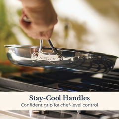 A hand lifts an EverLast Tri-Ply Clad Stainless Steel 12.5-Inch Frying Pan with Lid and Helper Handle above a stove burner. Text: “Stay-cool handles—Confident grip for home chef-level control.”.