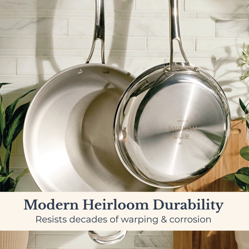 Two EverLast Tri-Ply Clad Stainless Steel Frying Pans hang on a tiled kitchen wall with green plants and a wooden cutting board. Text reads: Frying Pan Set—Modern Heirloom Durability that resists decades of warping & corrosion.