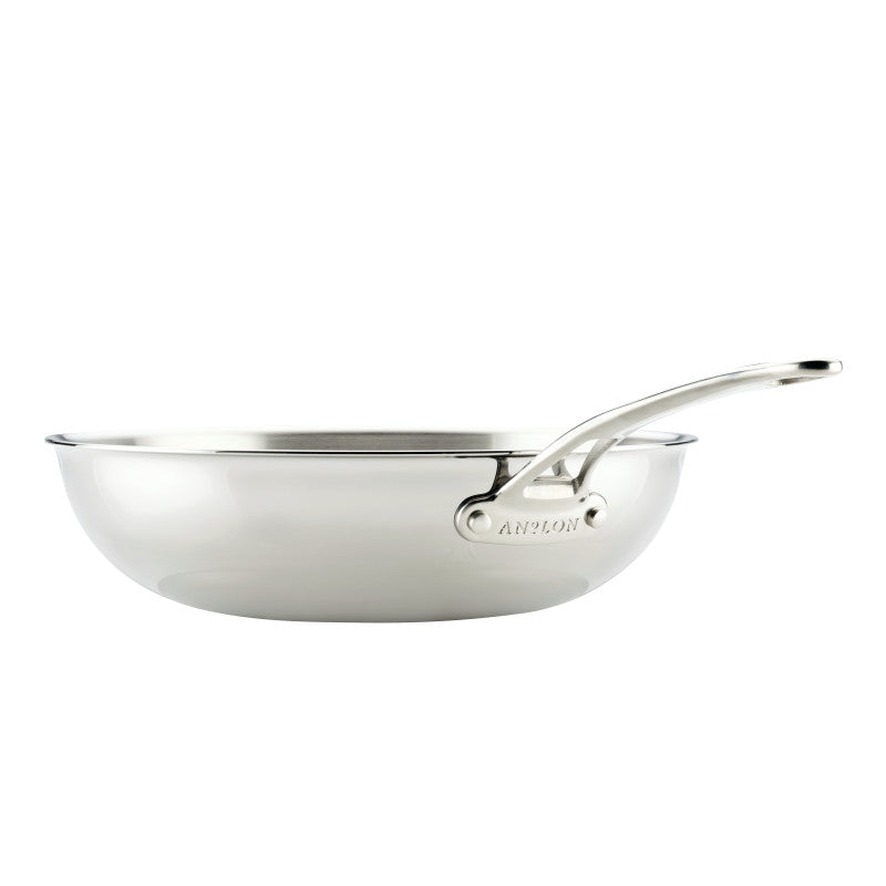 The EverLast Tri-Ply Clad Stainless Steel 12.25-Inch Stir Fry pan features a long, riveted handle and helper handle, plus smooth, curved edges—a shiny, reflective pan perfect for any home chef, shown from the side on a white background.