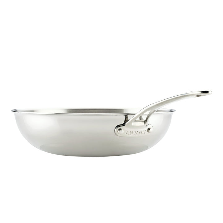 The EverLast Tri-Ply Clad Stainless Steel 12.25-Inch Stir Fry pan features a long, riveted handle and helper handle, plus smooth, curved edges—a shiny, reflective pan perfect for any home chef, shown from the side on a white background.