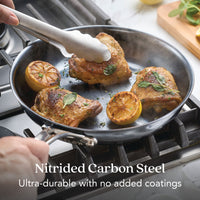 A person cooks seasoned chicken thighs and lemons in the 10-Inch N₂ Carbon Steel Frying Pan by N₂ Carbon Steel. Ultra-durable, rust resistant, and develops a natural nonstick patina with use.