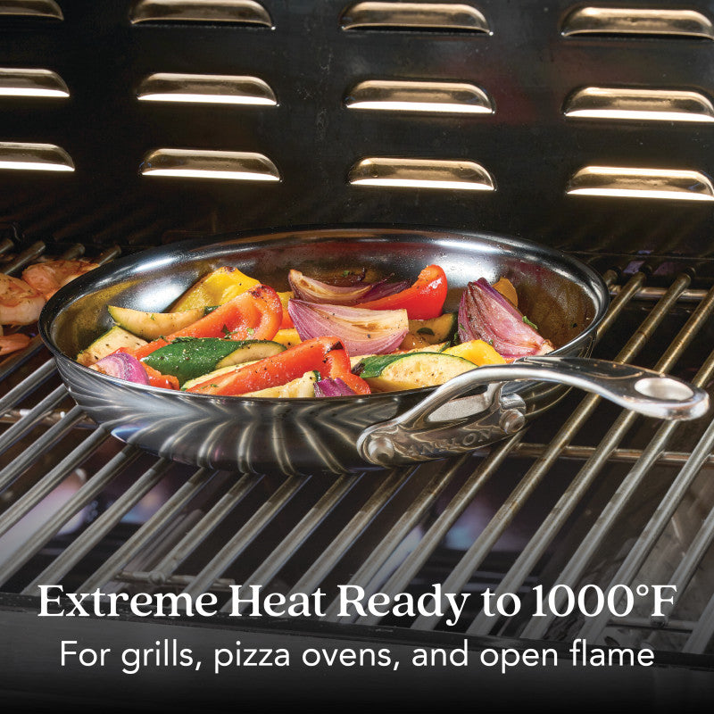 A N₂ Carbon Steel 10-Inch Frying Pan, featuring a nonstick patina and rust resistance, is filled with grilled vegetables on a grill rack inside an oven. Text: Extreme Heat Ready to 1000°F. For grills, pizza ovens, and open flame.
