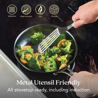 A person uses a metal spatula to cook veggies in the 10-Inch N₂ Carbon Steel Frying Pan by N₂ Carbon Steel on an induction cooktop. Metal utensil friendly, rust resistant, nonstick patina. Works on all stovetops, including induction.