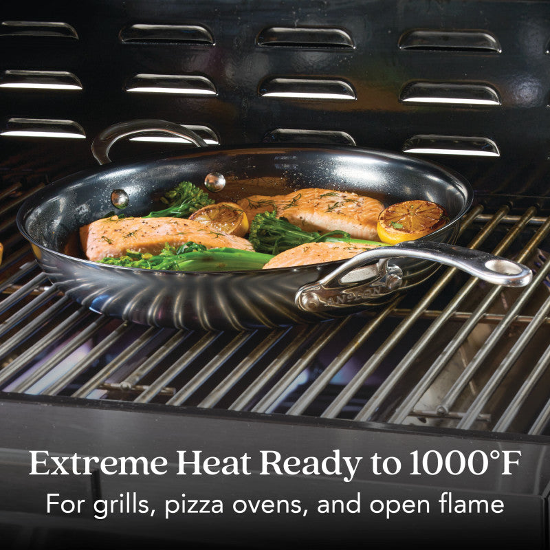 The 12-Inch N₂ Carbon Steel Frying Pan by N₂ Carbon Steel cooks salmon, lemon slices, and greens on a grill. Extreme heat ready up to 1000°F for grills, pizza ovens, and open flames with a naturally evolving nonstick surface.