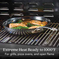The 12-Inch N₂ Carbon Steel Frying Pan by N₂ Carbon Steel cooks salmon, lemon slices, and greens on a grill. Extreme heat ready up to 1000°F for grills, pizza ovens, and open flames with a naturally evolving nonstick surface.