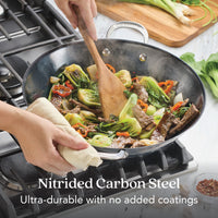A person stir-fries veggies and beef in the N2 Carbon Steel Wok by N2 Carbon Steel on a gas stove, using a wooden spatula and holding the handle with a cloth. Text: Natural nonstick patina. Ultra-durable, no added coatings.