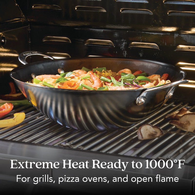 The N2 Carbon Steel Wok by N2 Carbon Steel is shown on a grill, filled with stir-fried veggies and shrimp. Text reads: “Extreme Heat Ready to 1000°F. For grills, pizza ovens, and open flame.”.