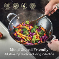 A hand stirs vibrant veggies in the N2 Carbon Steel Wok on a stovetop. This nitrided, metal utensil friendly wok from N2 Carbon Steel is compatible with induction, glass-ceramic, gas, and electric cooktops.