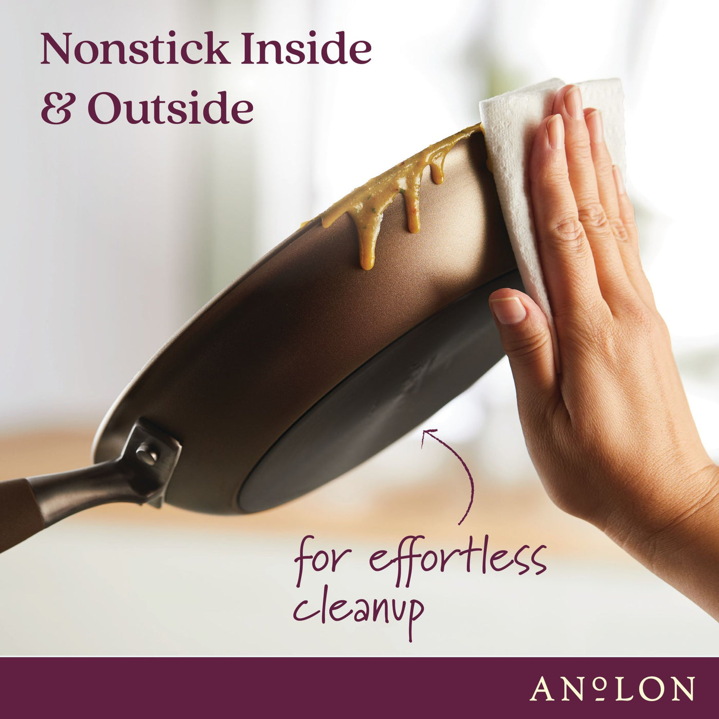 A hand wipes a nonstick frying pan with a paper towel. The pan has a mess on the exterior but is easily cleaned. Text: Nonstick Inside & Outside for effortless cleanup. The image promotes ANOLON cookware.