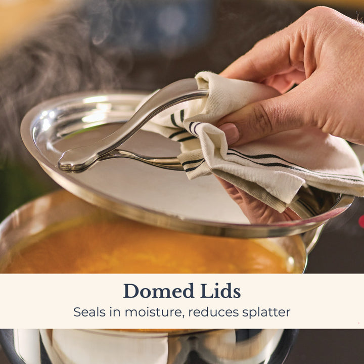 A hand lifts the domed lid from a steaming Nouvelle Stainless 2.5-Quart Saucier, with text: Domed Lids - Seal in moisture, reduce splatter.
