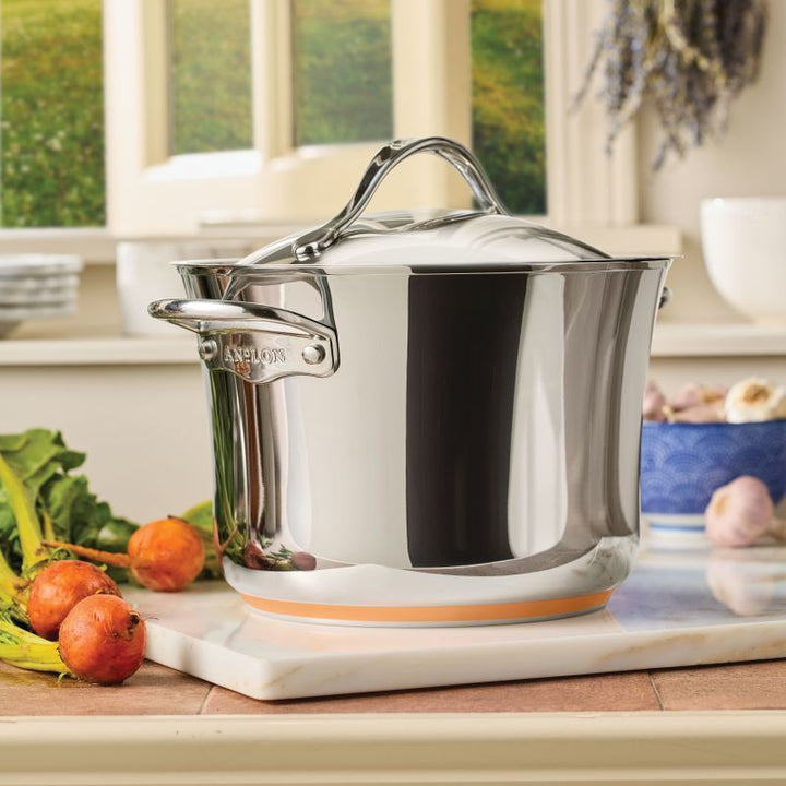 A Nouvelle Stainless 6.5-Quart Stockpot with Lid sits on a marble cutting board in a bright kitchen, surrounded by fresh beets, greens, and a blue bowl of garlic in the background.