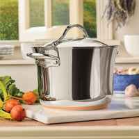 A Nouvelle Stainless 6.5-Quart Stockpot with Lid rests on a kitchen counter, surrounded by fresh vegetables and garlic, while sunlight filters through a window with greenery—a perfect showcase for quality cookware.