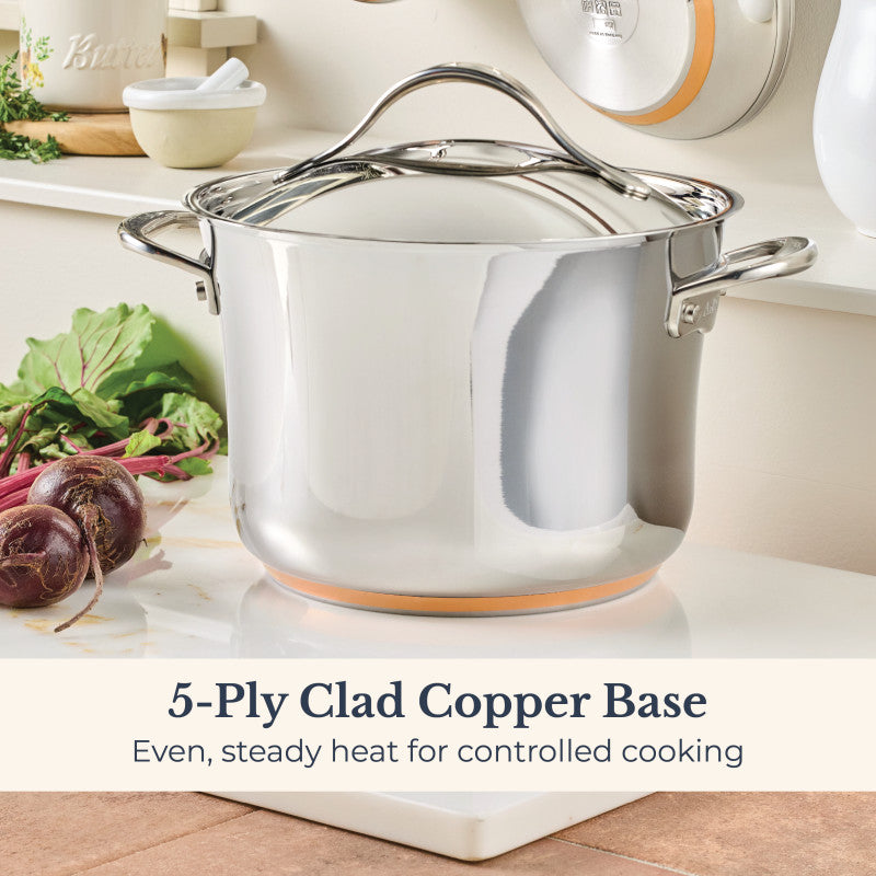 A Nouvelle Stainless 6.5-Quart Stockpot with Lid sits on a white surface next to purple onions and green leafy veggies. Text reads: “5-Ply Clad Copper Base. Even, steady heat for controlled cooking.”.