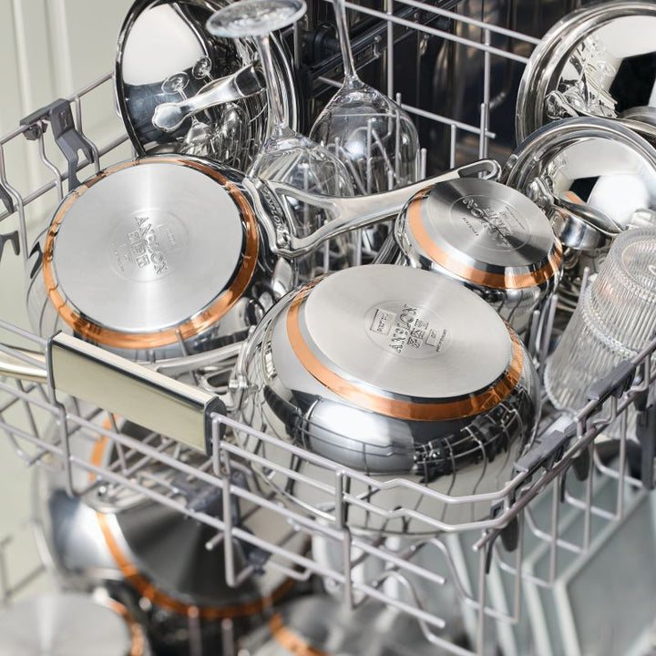 Open dishwasher filled with shiny cookware, including a Nouvelle Stainless 6.5-Quart Stockpot with Lid, copper pans, glassware, and cooking utensils neatly arranged on the racks.