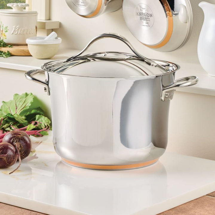 A Nouvelle Stainless 6.5-Quart Stockpot with Lid sits on a kitchen counter near fresh beets, with cookware and utensils visible in the background.