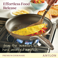 A pan on a stove holds an omelet with sliced vegetables. A spatula lifts the omelet, showing the nonstick surface. The text reads, Effortless Food Release and from the inventors of hard anodized nonstick, with Anolon branding.