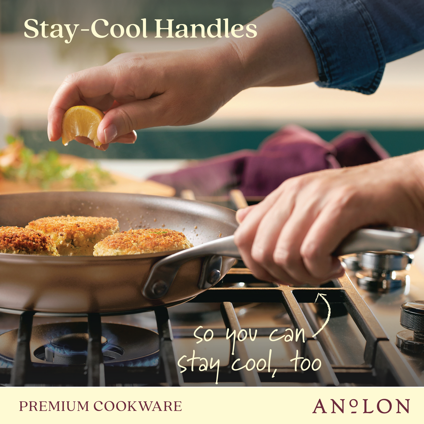 A person squeezes lemon juice over sizzling crab cakes in a pan on a stovetop. Text reads Stay-Cool Handles and so you can stay cool, too with the brand name Anolon at the bottom. A kitchen towel is visible in the background.