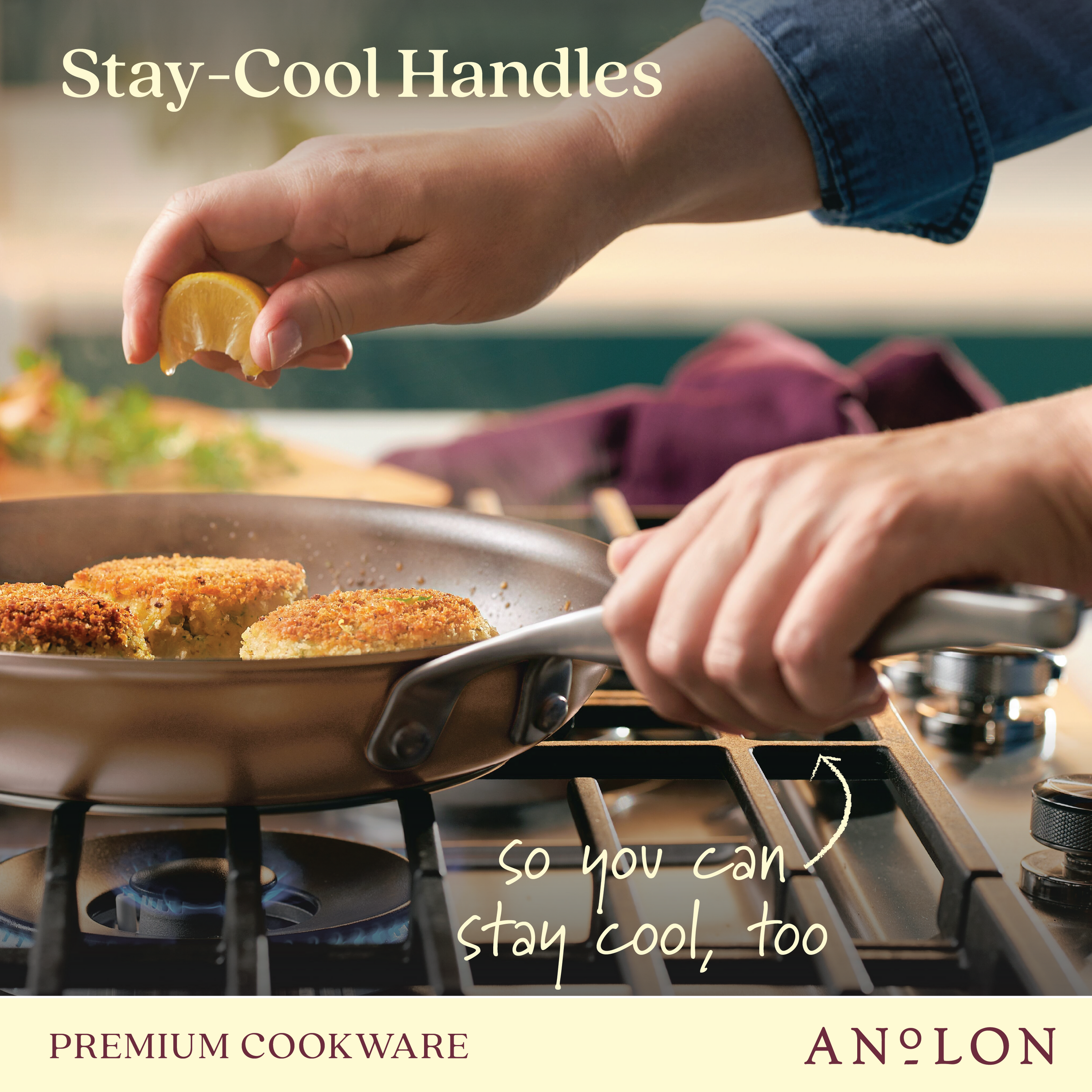 A person squeezes lemon juice over sizzling crab cakes in a pan on a stovetop. Text reads Stay-Cool Handles and so you can stay cool, too with the brand name Anolon at the bottom. A kitchen towel is visible in the background.