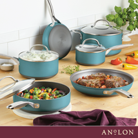 A kitchen scene with various teal pots and pans from Anolon, containing foods like mashed potatoes, beef, and vegetables. The cookware is arranged on a wooden counter, with colorful bell peppers and herbs in the background.