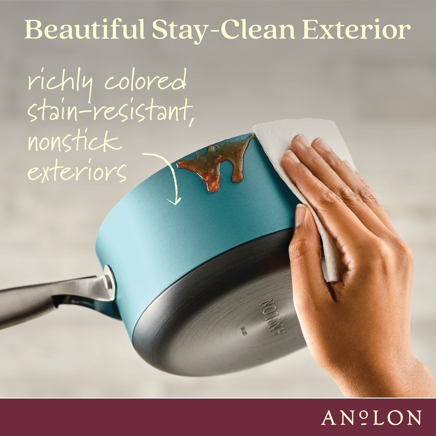 A hand wipes a stain off a blue pan with a white cloth. Text reads Beautiful Stay-Clean Exterior, highlighting the pans stain-resistant and nonstick exterior. The bottom right corner has the brand name Anolon.