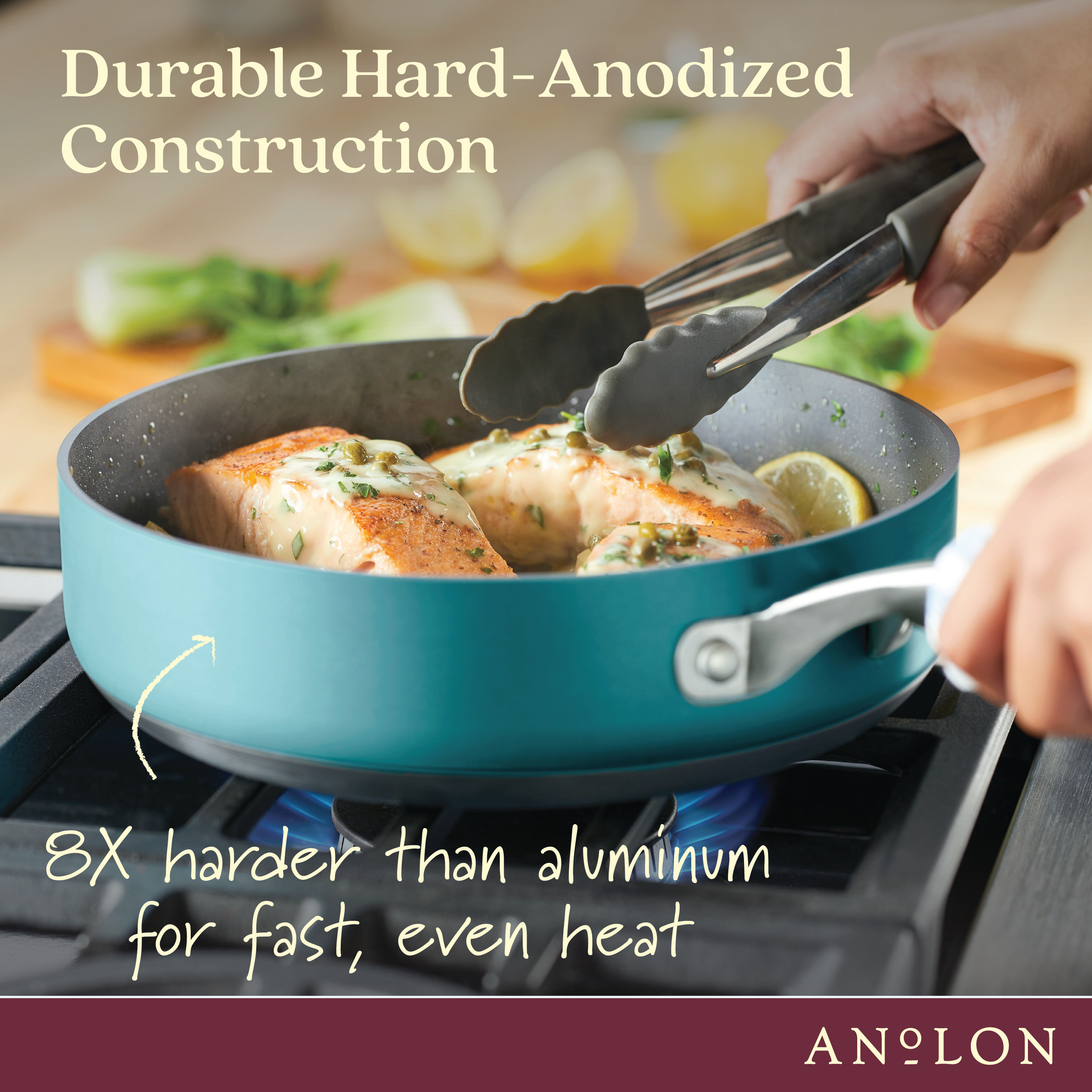 A person uses tongs to cook salmon fillets in a teal, hard-anodized pan on a stovetop. Text reads: Durable Hard-Anodized Construction. 8X harder than aluminum for fast, even heat. ANOLON logo is at the bottom.
