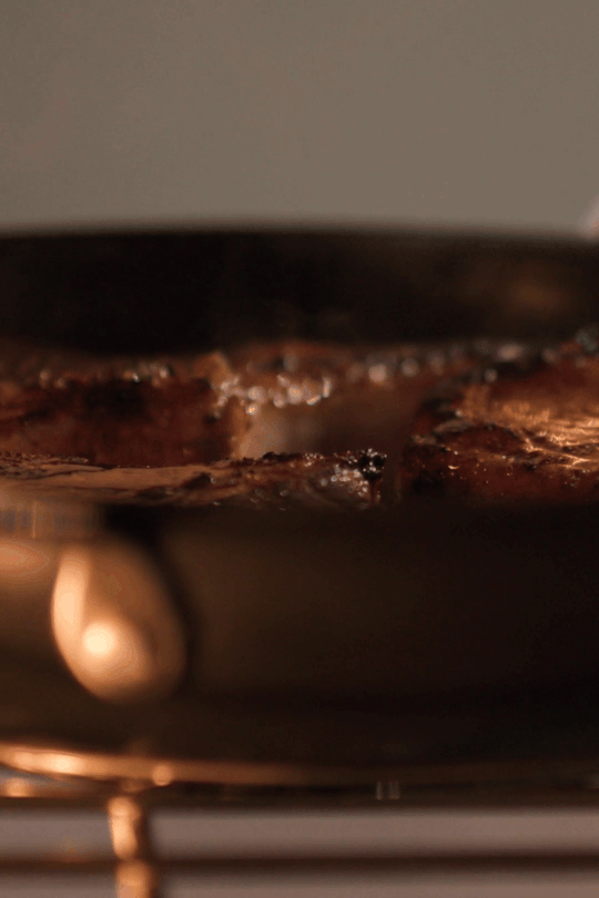 A vertical looping GIF showing an Anolon X frying pan being lifted out of a hot oven. The pan contains a seared pork tenderloin topped with a vibrant blueberry reduction, highlighting the cookware's oven-safe durability and its ability to transition from high-heat searing to oven roasting.