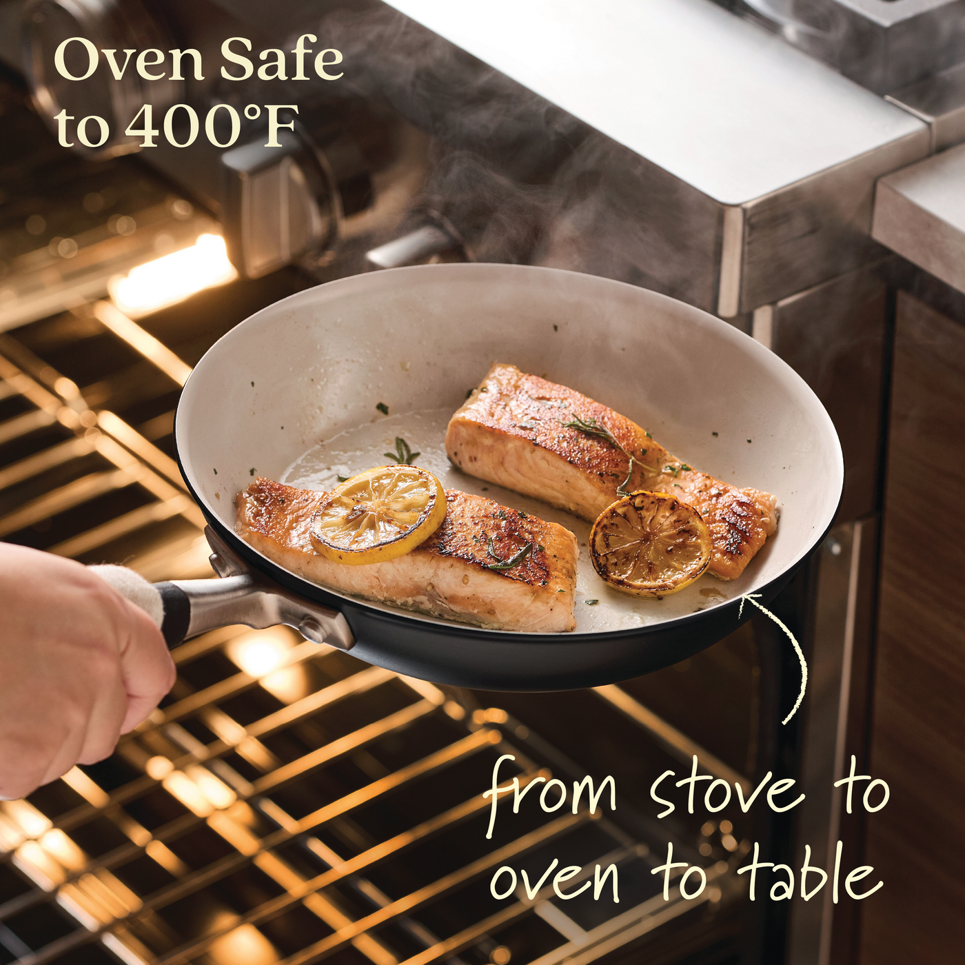 A hand holds a pan with two salmon fillets and lemon slices, highlighting the Oven Safe to 400°F feature of the Anolon Advanced Ceramic 2-Piece Nonstick Frying Pan Set, designed for quality performance from stove to oven to table.