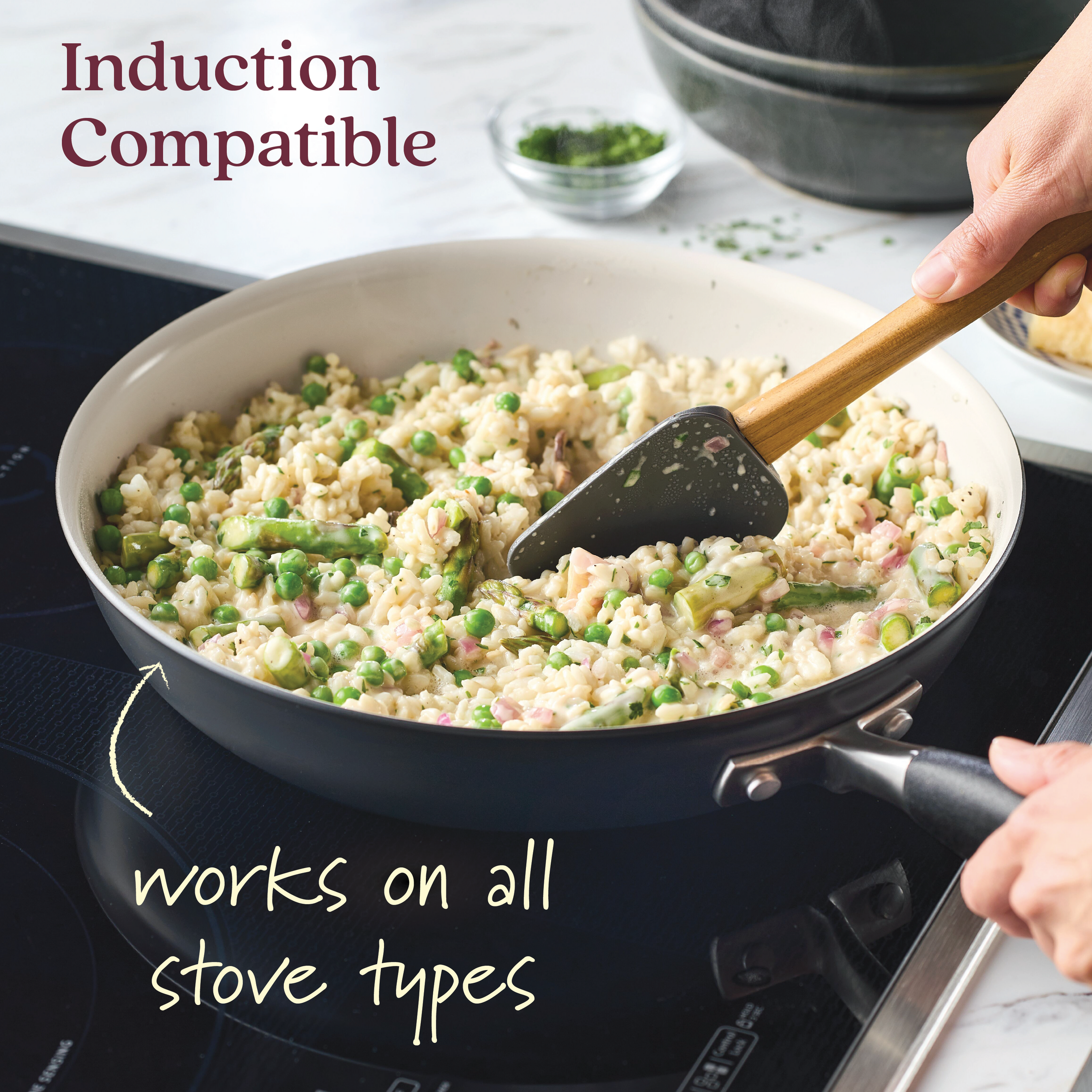 An Advanced Ceramic 12-inch Nonstick Frying Pan is used to stir risotto with peas on an induction stove. The text Induction Compatible and works on all stove types is visible, while a bowl of chopped herbs waits in the background to be added for flavor.