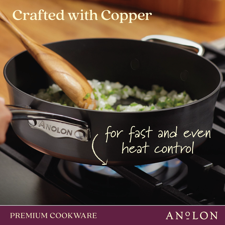 A close-up of a 12-Inch Stir Fry from Nouvelle Copper Luxe on a gas stove with onions and green vegetables being stirred by a wooden spoon. Copper craftsmanship and premium nonstick ensure fast, even heat control. Induction suitable.
