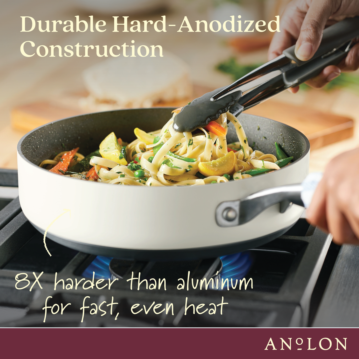 Person cooking pasta with vegetables in a white pan using tongs on a stovetop. Text reads Durable Hard-Anodized Construction and 8X harder than aluminum for fast, even heat.