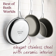 Three shiny pans hang against a white tiled wall, showcasing the EverLast Ceramic Stainless Steel set with its stainless steel exteriors and ceramic nonstick interiors. Text reads, Best of Both Worlds, featuring the blend of clad stainless steel and efficient heating for superior cooking performance.