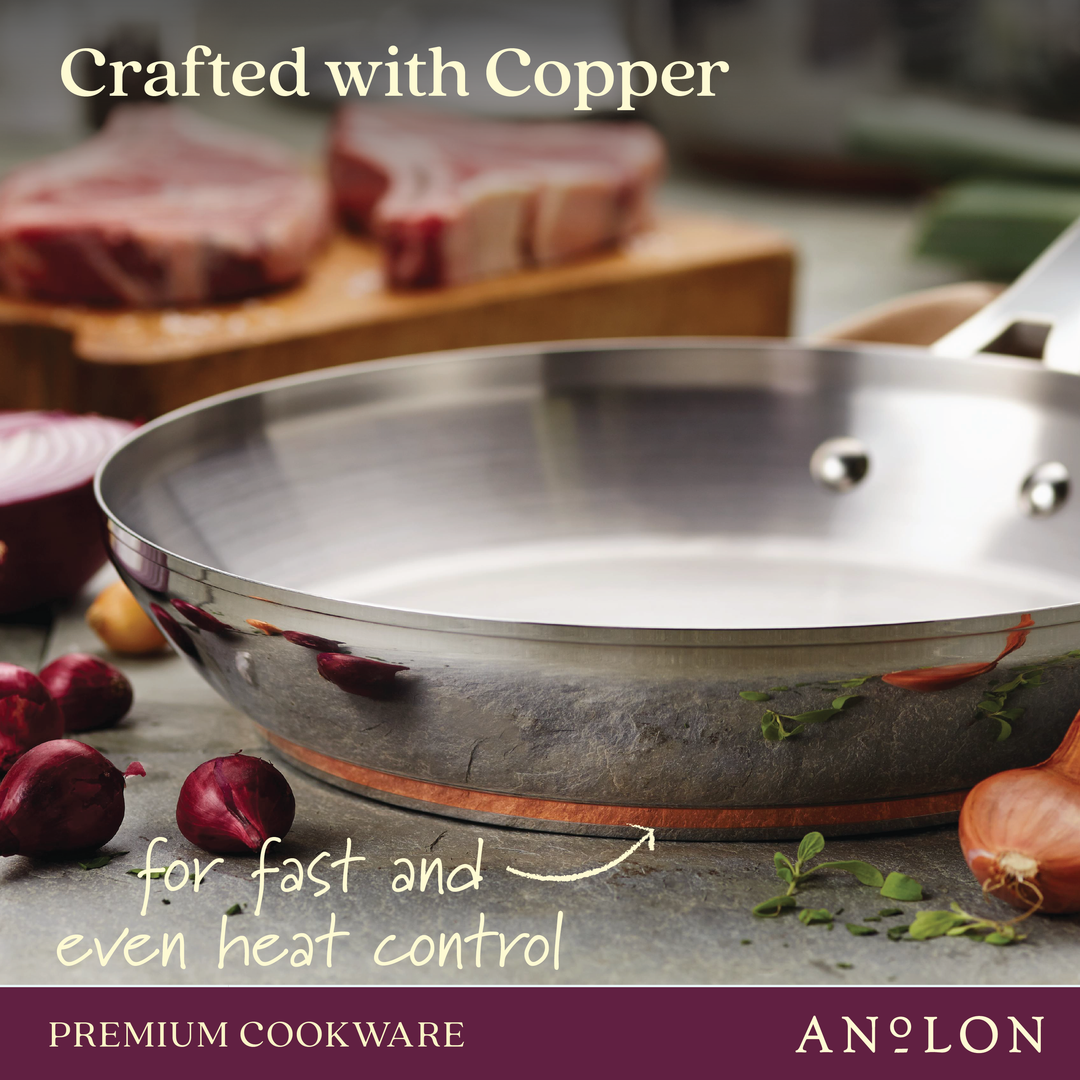 Close-up of a copper-bottomed frying pan from the Nouvelle Luxe 11-Piece Mixed Metals Cookware Set on a kitchen counter, surrounded by sliced red onions and herbs. In the background, blurred slabs of raw meat are visible. Text reads: Crafted with copper and stainless steel for fast and even heat control. Premium Cookware - Nouvelle Luxe.