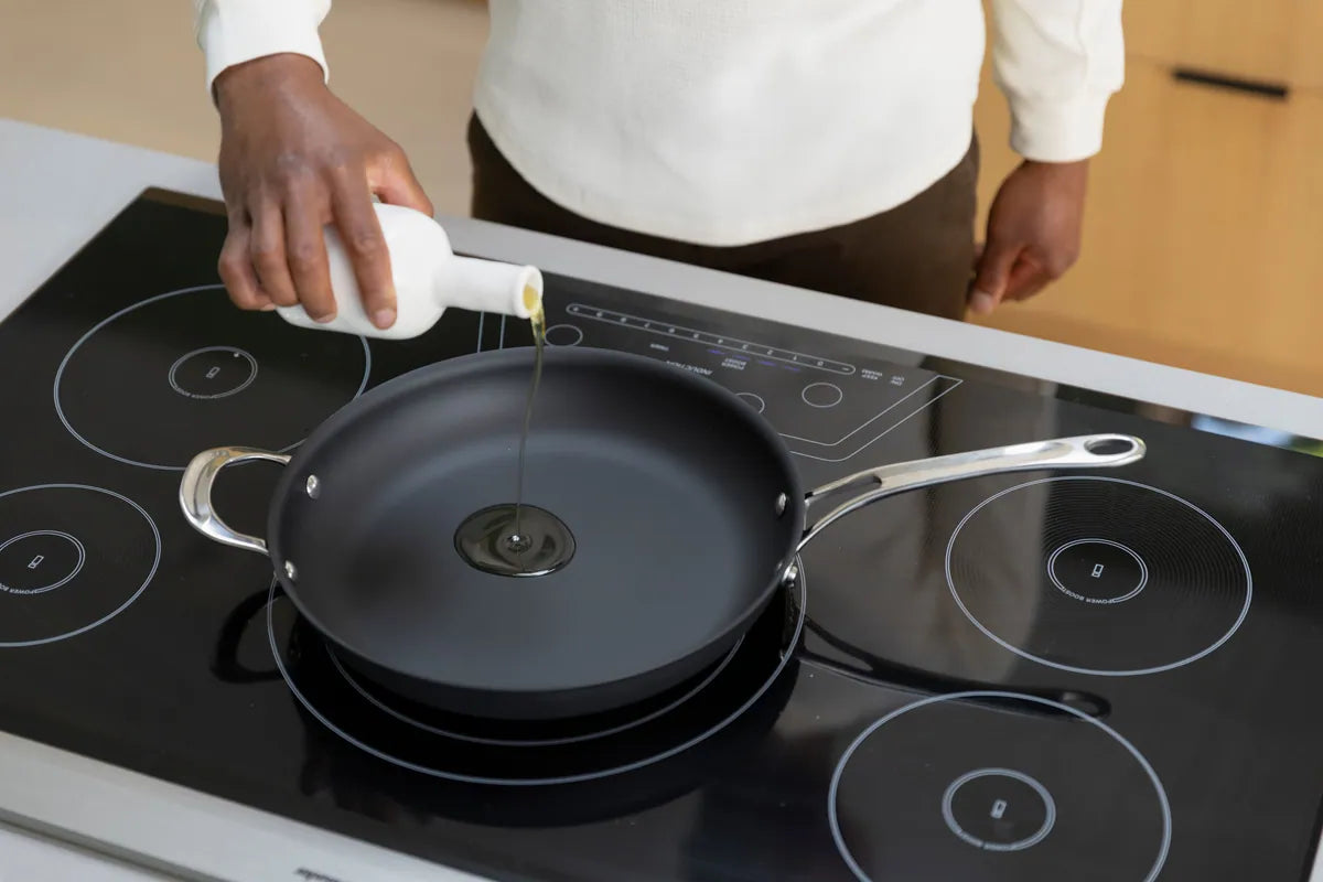 Hand pouring oil onto carbon steel pan set on top of an induction cooktop