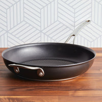 The Anolon X 12-Inch Hybrid Nonstick Frying Pan by Anolon X, featuring a metal handle and metal utensil-safe, ultra-durable nonstick surface, rests on a wooden countertop with a geometric gray and white backsplash behind.