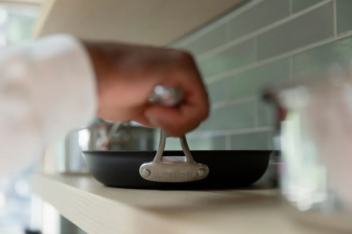 Hand holding the handle of a carbon steel pan and setting it on a kitchen shelf