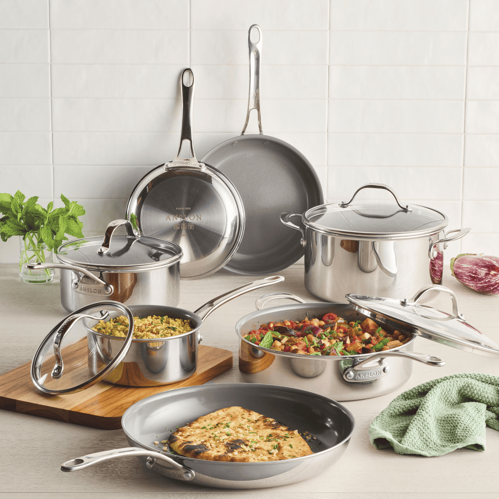 Displayed on a kitchen counter, the 11-Piece Ceramic Nonstick Stainless Steel Cookware Set by EverLast features various pots and pans. One pan holds a savory dish, another a frittata. Fresh herbs and utensils are nearby against a white tiled backsplash, promising efficient heating for every meal.