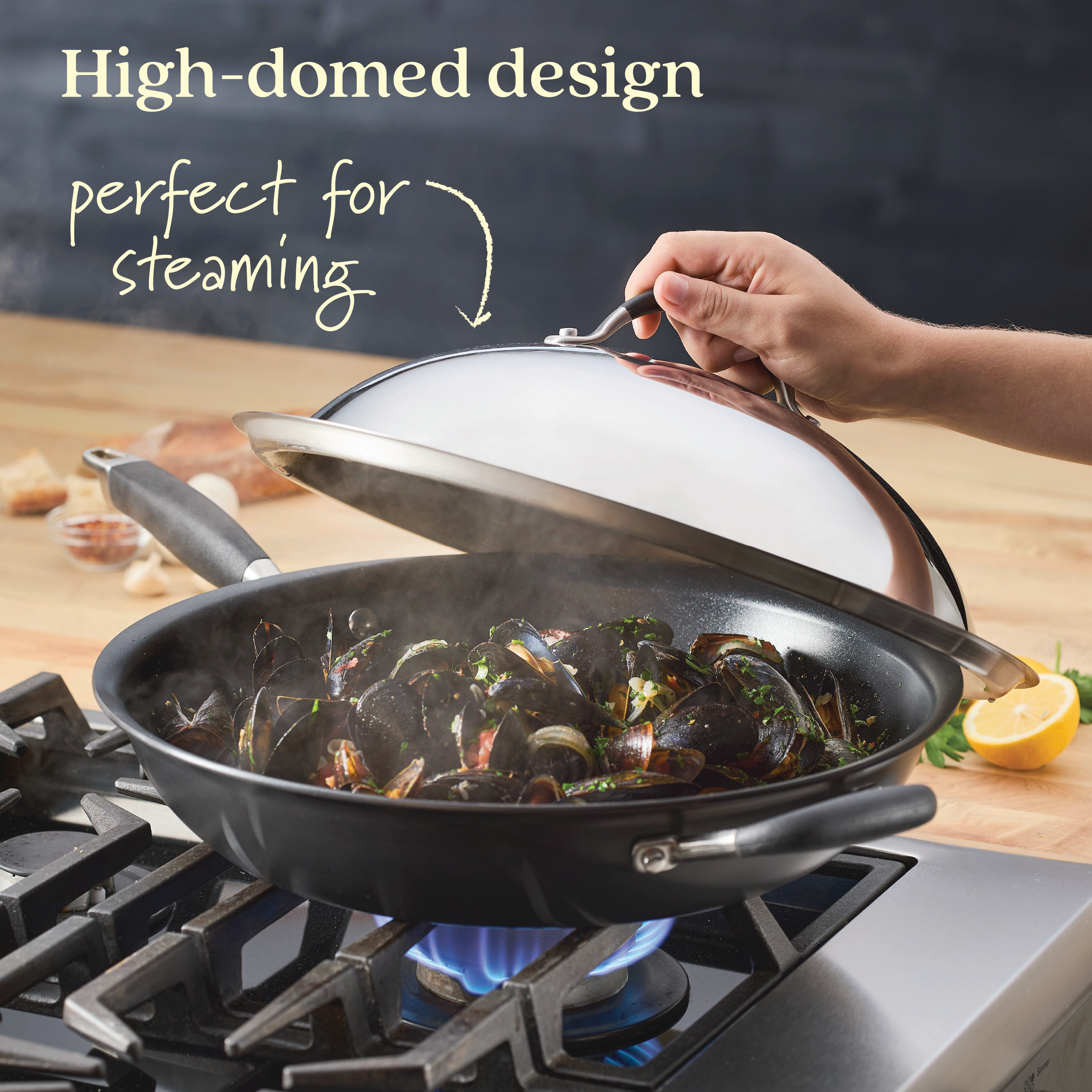 A person lifts the 14-Inch Stainless Steel Domed Lid from Advanced Home off a frying pan on a stove, revealing steaming mussels inside. The background includes a cut lemon and garlic cloves. Text reads: Designed for perfect steaming and built to last with durable craftsmanship.