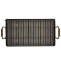 A rectangular baking pan with a wire rack resting inside. The pan has two handles on the shorter sides, each with a brown grip. The rack is metal, consisting of parallel bars running the length of the pan.